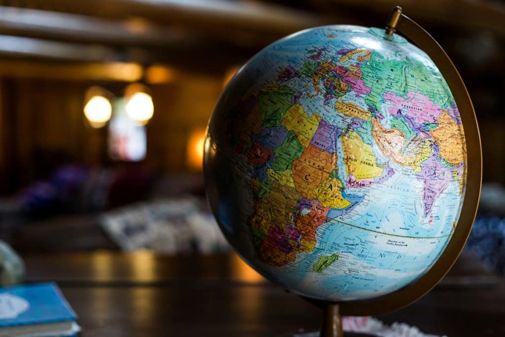 A globe on a wooden table, focusing on Africa and Europe, invites daydreams of travel. In the dimly lit room with cozy ambiance, two lights softly glow in the blurred background. It's a perfect setting to ponder how early you should start planning for spring break adventures.