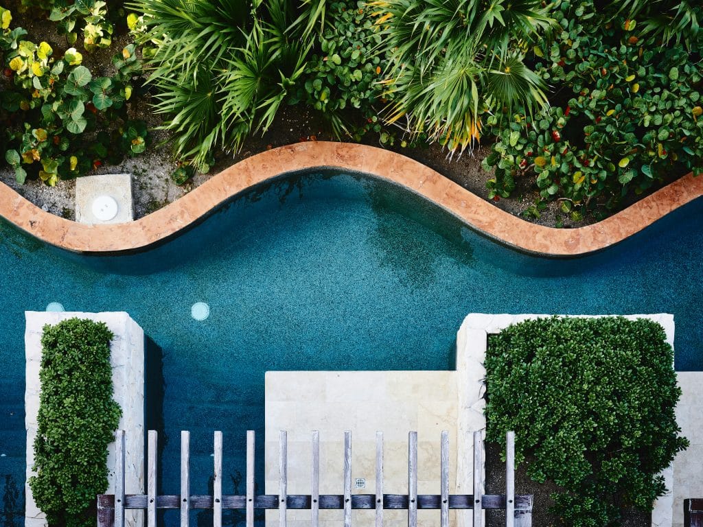 Top view of a curved swimming pool surrounded by lush green plants and shrubs. The pool features a light-colored stone border with a small fountain visible. Secrets Playa Mujeres Golf & Spa Resort, Cancún, Mexico