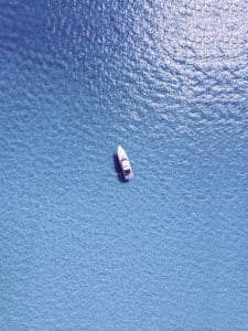 Aerial view of a small white boat floating on a vast expanse of calm, blue water under sunlight.