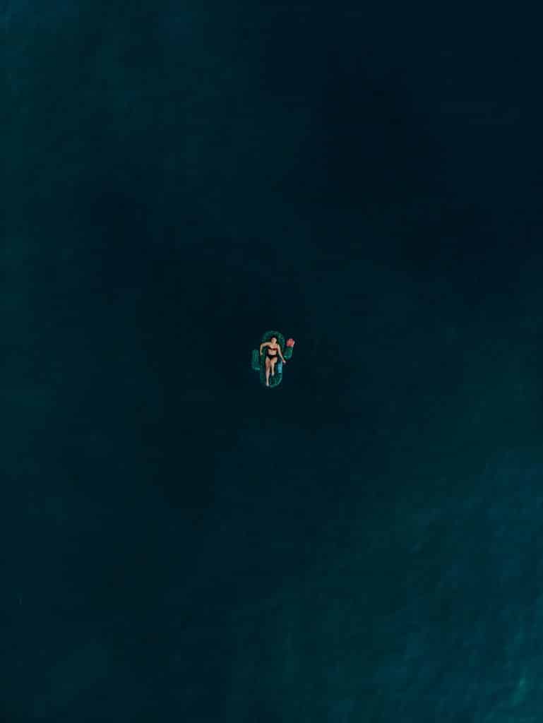 A person floats on their back in deep, dark water. They are centered in the image, surrounded by a vast expanse of water, creating a sense of isolation and tranquility.